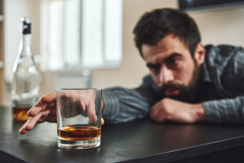 drunk man reaching for glass of whiskey on table.