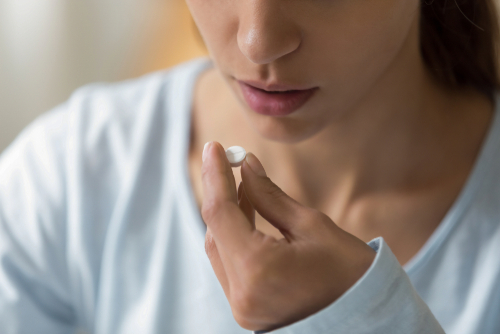 Closeup of a woman's face and pill in hand about to take it.