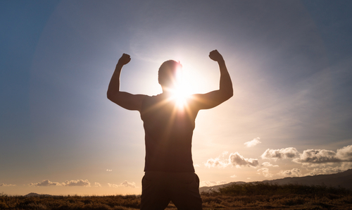 Silhouette of healthy young man flexing indicating triumph over a hardship.